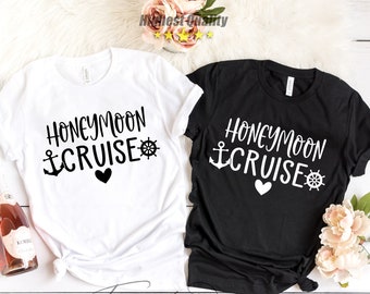 May include: Two t-shirts with the text "Honeymoon Cruise" in black lettering. The shirts are white and black. The white shirt has a black anchor and steering wheel. The black shirt has a white anchor and steering wheel. Both shirts have a small black heart.