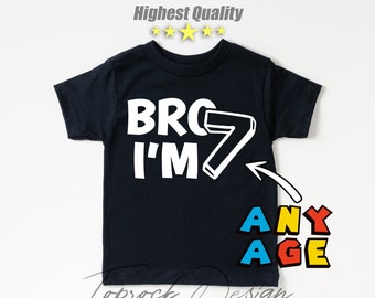 May include: Black t-shirt with white text that reads "Bro I'm 7" with a white number 7. The number 7 is outlined in black and has a red, yellow, and blue arrow pointing to the text "Any Age" in red, yellow, and blue.