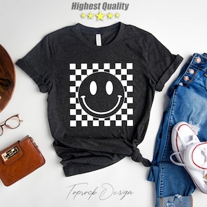 May include: A dark gray t-shirt with a white smiley face on a black and white checkered background. The text "Topsock Design" is printed on the bottom of the shirt.