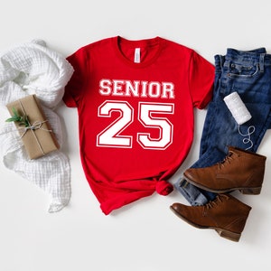 May include: Red t-shirt with white text that says "Senior 25" in a varsity style font.