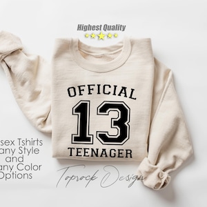 May include: A beige sweatshirt with black text that reads "OFFICIAL 13 TEENAGER".
