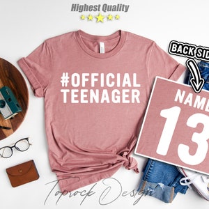 May include: A pink t-shirt with the text "#OFFICIAL TEENAGER" in white. A separate pink square with the text "NAME 13" in white.