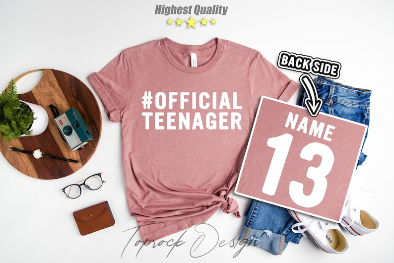 May include: A pink t-shirt with the text "#OFFICIAL TEENAGER" in white. A separate pink square with the text "NAME 13" in white.