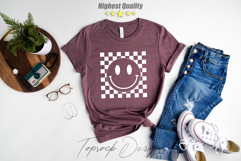 May include: A maroon t-shirt with a white checkered pattern and a white smiley face in the center. The text "Toprock Design" is visible in the bottom right corner of the image.