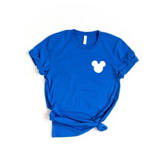 Puede incluir: Una camiseta azul real con una silueta blanca de Mickey Mouse en el pecho izquierdo.