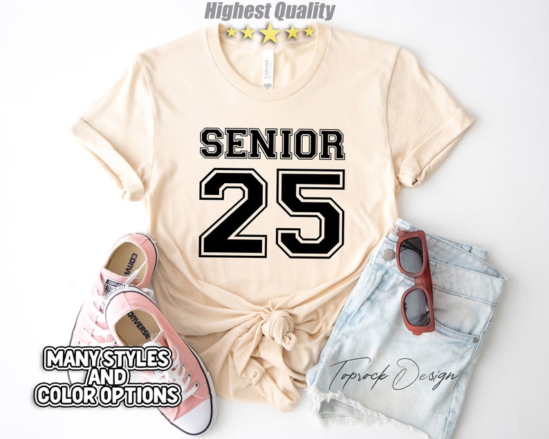 May include: A beige t-shirt with black text that says "Senior 25" in a varsity style font.