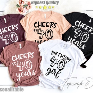 May include: Five different t-shirts with various birthday designs. The shirts are in different colors, including maroon, peach, black, and white. The text on the shirts reads "Cheers to 40 years" and "Birthday 40 girl".