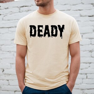 May include: A light beige t-shirt with a black graphic that says "DEADLY" in dripping letters.