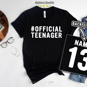 May include: Black t-shirt with white text that says "#OFFICIAL TEENAGER". The back of the shirt has a white number "13" with the word "NAME" above it.