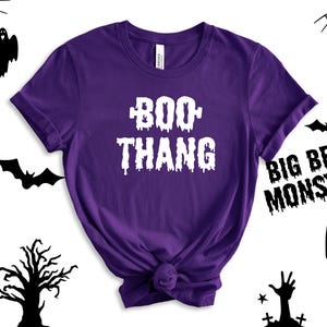 May include: Purple short-sleeved t-shirt with the text "BOO THANG" in white dripping letters.