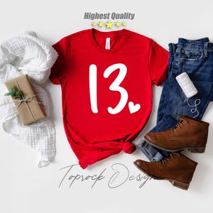 May include: Red t-shirt with white text that says "13" with a small heart next to it.  The shirt is on a white background.