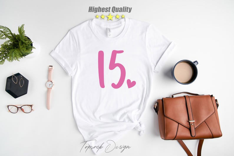 May include: White t-shirt with pink lettering that says "15."  There is a small pink heart next to the number.