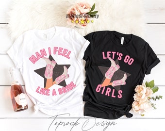 May include: Two white and black t-shirts with pink text and a graphic of a pair of pink cowboy boots. The white shirt says "Man I feel like a bride" and the black shirt says "Let's go girls".