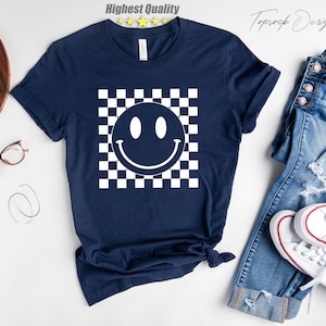 May include: A navy blue t-shirt with a white checkered pattern and a white smiley face in the center.