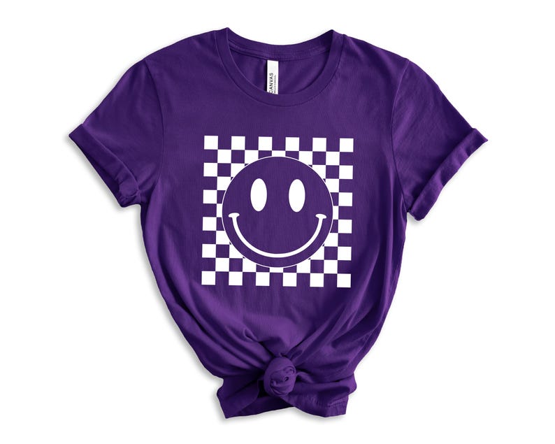 May include: Purple short-sleeved t-shirt with a white checkered pattern and a white smiley face graphic.