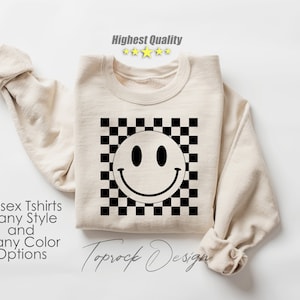 May include: A beige sweatshirt with a black and white checkered pattern and a black smiley face graphic. The text "Toprock Design" is printed on the bottom of the sweatshirt.