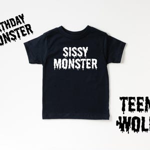 May include: Black t-shirt with white text that reads "Sissy Monster".