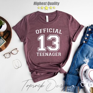 May include: A maroon t-shirt with white text that reads "OFFICIAL 13 TEENAGER".
