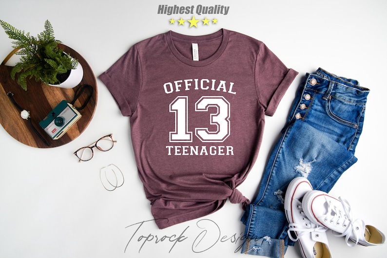May include: A maroon t-shirt with white text that reads "OFFICIAL 13 TEENAGER".