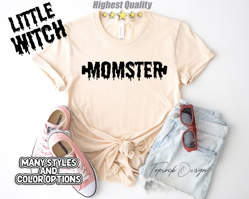May include: A light beige t-shirt with black dripping text that says "MOMSTER". The shirt is paired with denim shorts and pink Converse shoes.
