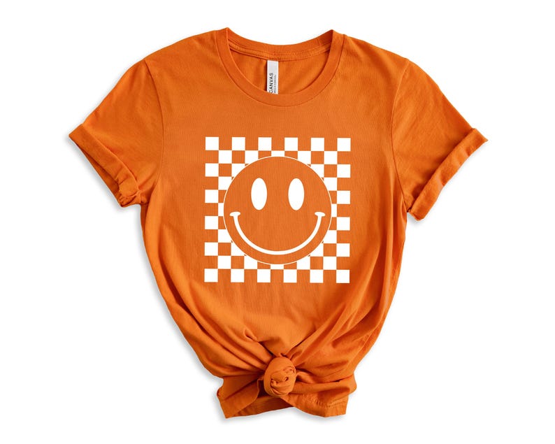 May include: Orange t-shirt with a white smiley face in a checkered pattern.