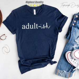 May include: A navy blue t-shirt with the text "adult-ish" printed in white on the front.
