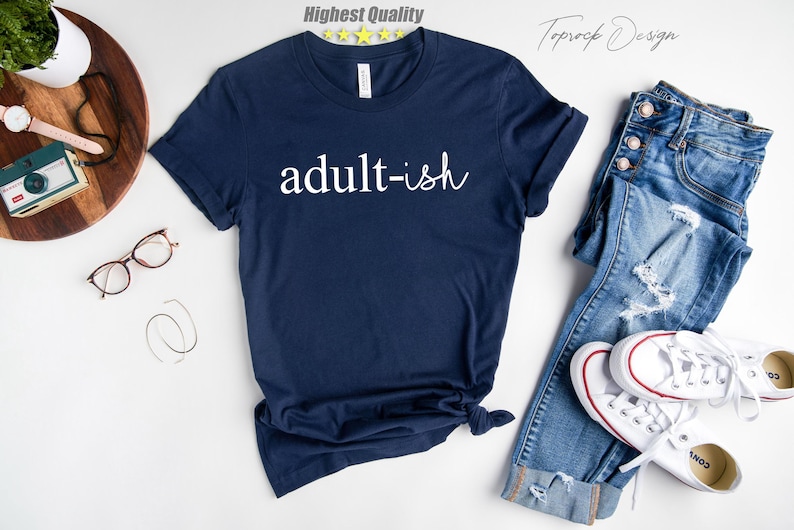 May include: A navy blue t-shirt with the text "adult-ish" printed in white on the front.
