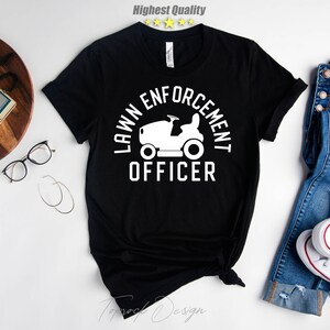May include: Black t-shirt with a white graphic of a lawnmower and the text "Lawn Enforcement Officer".