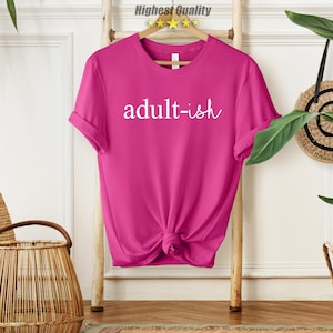 May include: A pink t-shirt with the text "adult-ish" in white lettering.