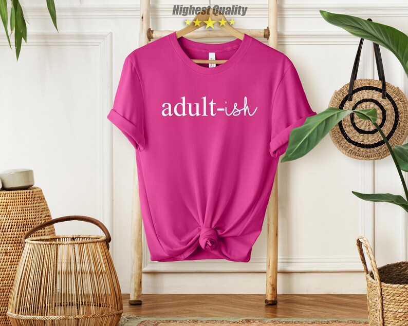 May include: A pink t-shirt with the text "adult-ish" in white lettering.