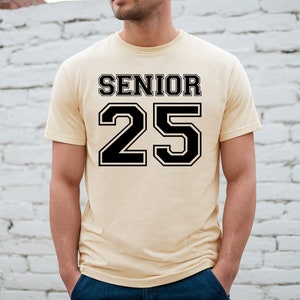 May include: A light yellow t-shirt with black text that says "Senior 25" in a varsity style font.