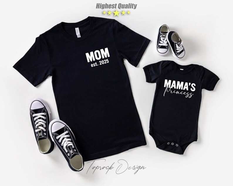 May include: Black t-shirt with "MOM est. 2025" text and a black baby onesie with "MAMA'S Princess" text. Two pairs of black and white canvas sneakers are also in the image. The image has a white background.
