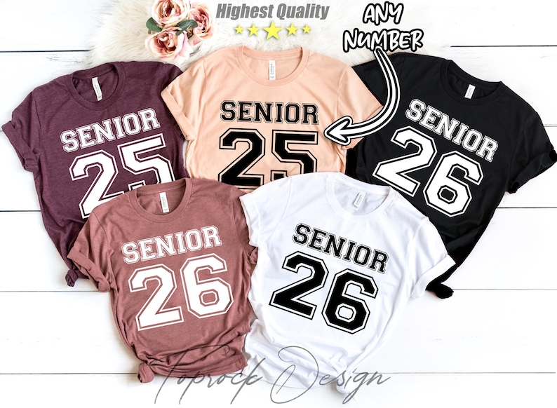 May include: Five t-shirts with the word "Senior" and a number printed on the front. The shirts are in different colors, including black, white, pink, and brown. The numbers are 25 and 26.