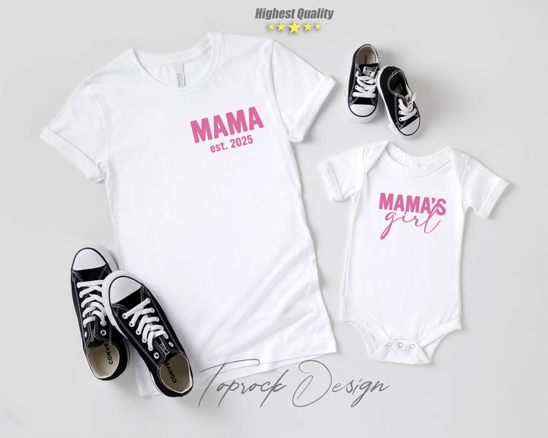 May include: White t-shirts and a baby onesie with pink text that reads "MAMA est. 2025" and "MAMA'S girl". Black and white sneakers are placed near the shirts. The image is a flat lay on a light gray surface.