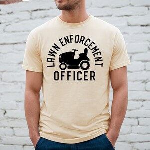 May include: A light yellow t-shirt with a black graphic of a lawnmower and the text "LAWN ENFORCEMENT OFFICER".