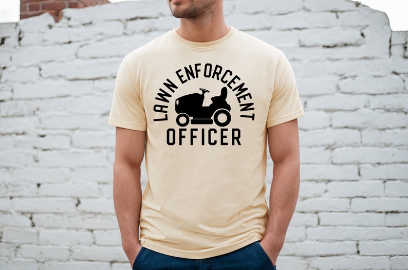 May include: A light yellow t-shirt with a black graphic of a lawnmower and the text "LAWN ENFORCEMENT OFFICER".