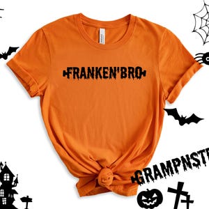 May include: Orange t-shirt with black dripping text that reads "Franken'Bro" and "Grampnstein".