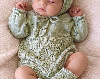 May include: A sage green knitted baby outfit consisting of a long-sleeved romper with a leaf-patterned texture, a matching bonnet with a tie closure, and a pair of soft knitted booties. The set features ribbed cuffs and a delicate knit design.