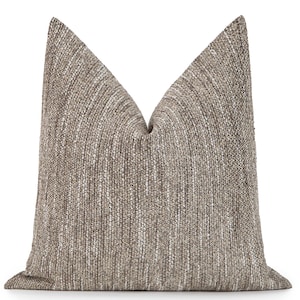 May include: A decorative throw pillow with a textured, woven fabric in shades of brown and white. The pillow has a neutral color palette and a soft, inviting appearance, suitable for home decor.