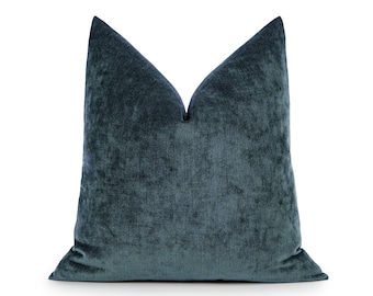May include: A square throw pillow cover in a deep teal blue color. The fabric has a textured, velvet-like appearance with a subtle sheen that catches the light. The pillow is plumped at the top to create a distinct V-shaped indentation.