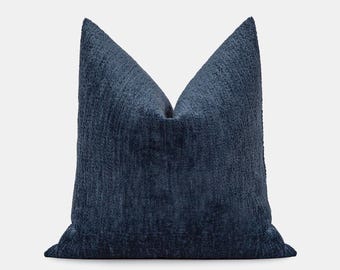 Könnte beinhalten: Ein quadratisches, marineblaues Zierkissen mit einem strukturierten, gewebten Stoff. Das Kissen hat ein weiches, plüschiges Aussehen und ist für die Inneneinrichtung konzipiert. Die Abmessungen des Kissens sind auf dem Bild nicht sichtbar.