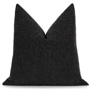 May include: A square throw pillow featuring a deep black fabric with a distinct, raised, and uniform textured weave. The pillow is plumped to create a sharp, pointed top center crease, showcasing the dense, tactile quality of the dark material.