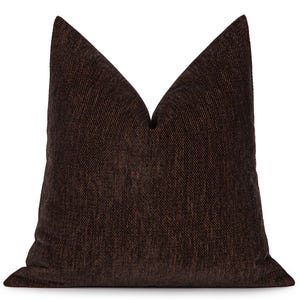 May include: A dark brown cushion with a textured weave. The cushion is square with a pointed top, suitable for a bed or sofa. The cushion is a solid colour and has a simple, elegant design. The measurements are in centimetres.