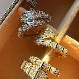 May include: Three pairs of gold and silver hoop earrings with baguette-shaped cubic zirconia stones. The earrings are arranged in a row in a jewelry box.
