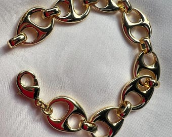 May include: A gold-toned chain bracelet featuring polished, rounded, oval-shaped links with a central horizontal bar in each link. The bracelet is secured with a lobster claw clasp, showcasing a smooth, reflective metallic finish throughout.