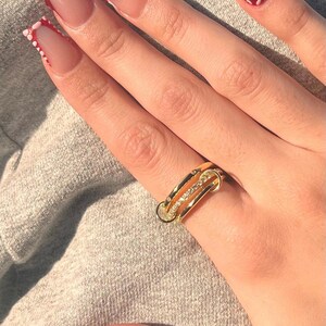 May include: A gold ring with three bands and small clear stones. The ring is on a person's finger with red and white nail polish.