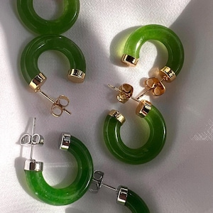 May include: Four pairs of green hoop earrings with gold and silver accents. The earrings are made of a smooth, green material and have a simple, elegant design.