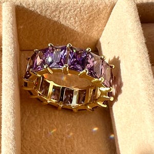 May include: A gold ring with a band of purple square-shaped stones.