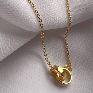 May include: A gold chain necklace with a pendant featuring two interlocking rings.