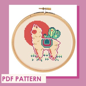 May include: Cross stitch pattern featuring a llama with a cactus on its back, set against a red sunset. The pattern is in a wooden embroidery hoop.